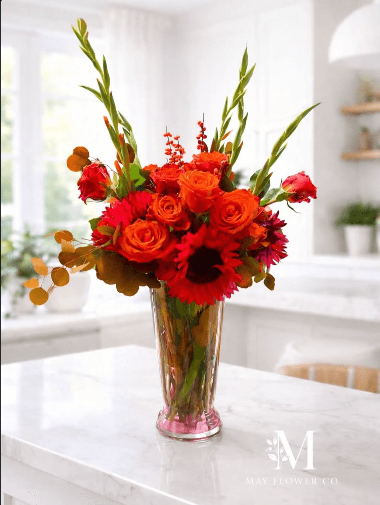 A bright orange arrangement of sunflowers and seasonal stems on a kitchen counter.