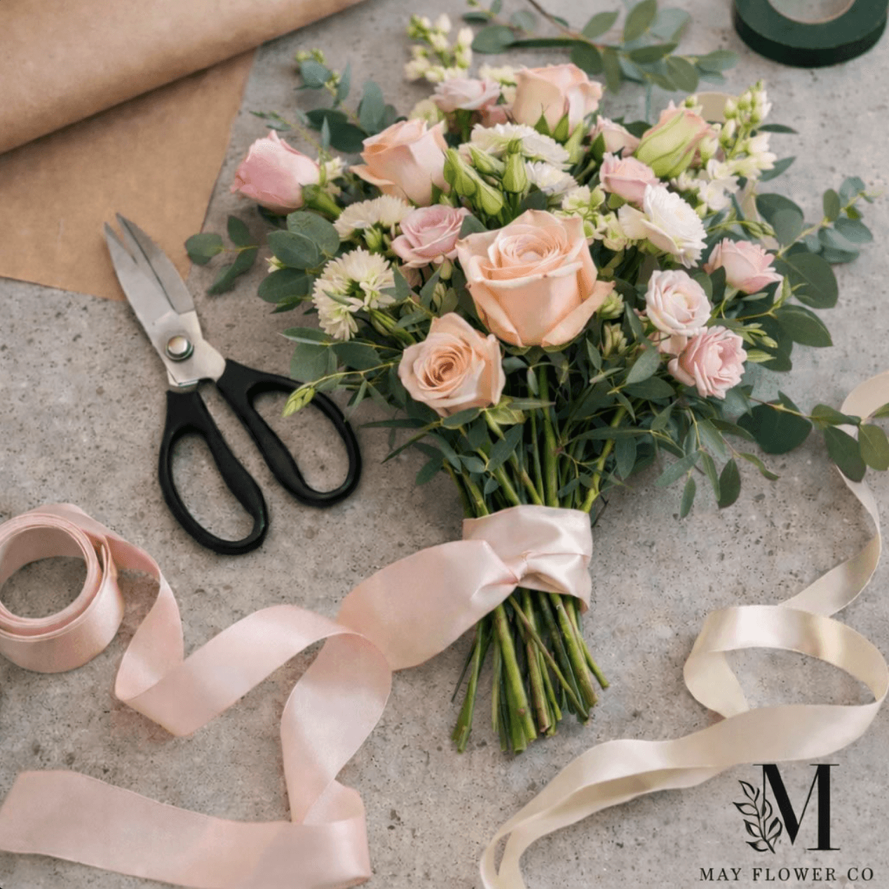 Overhead flat-lay of a bouquet, shears, and ribbons on a concrete floor.